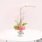 A vase filled with white orchid and pink flowers sits elegantly on a wooden table.