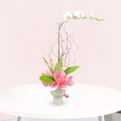 A vase filled with white orchid and pink flowers sits elegantly on a wooden table.