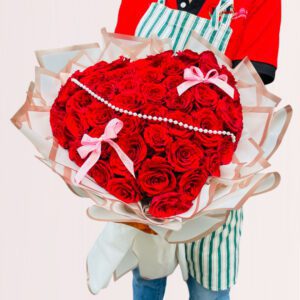 Make your loved one’s special occasion with this bouquet of red roses arranged in a heart shape and wrapped in decorative white and pink paper with frilled edges. The string of white pearls and small pink ribbon bows make it perfect for weddings, anniversaries, or Valentine’s Day.