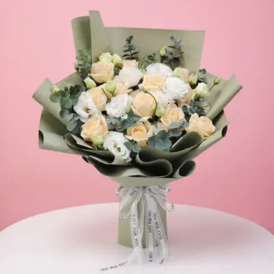Bouquet of peach roses and white eustoma with eucalyptus wrapped in olive green paper.
