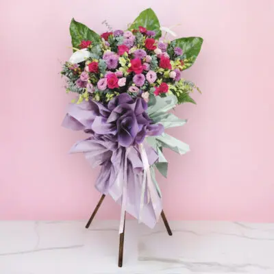 celebration flower stand with pink and purple roses, chrysanthemums, and a lavender ribbon.