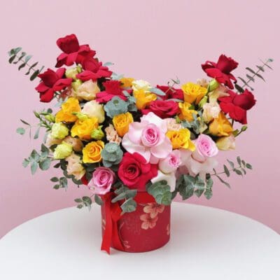 Mixed roses - red, pink, and yellow roses with eucalyptus in a red hatbox.