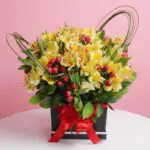 Yellow alstroemeria flower box with red berries and red ribbon in a black gift box.