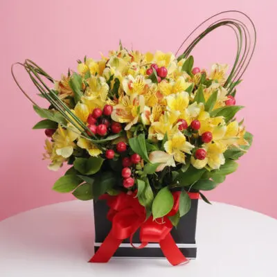 Yellow alstroemeria flower box with red berries and red ribbon in a black gift box.