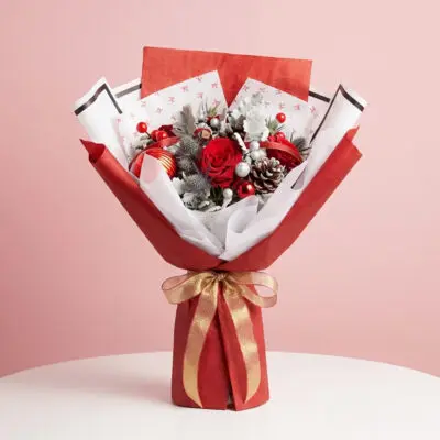 Christmas hand bouquet with red roses, berries, frosted leaves, silver ornaments in red-and-white wrapping.