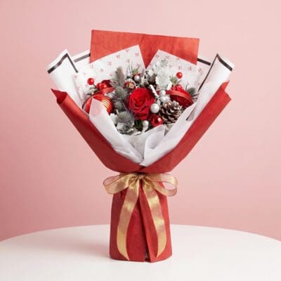 Christmas hand bouquet with red roses, berries, frosted leaves, silver ornaments in red-and-white wrapping.
