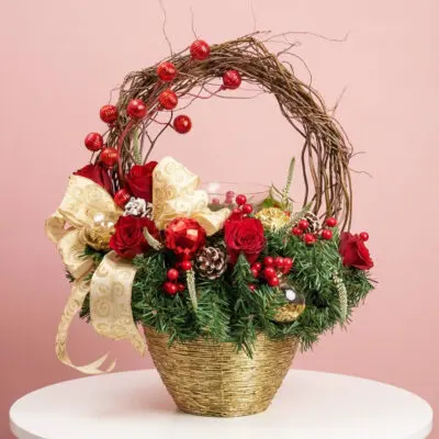 Christmas ring basket with red roses, pine cones, gold ribbon, red ornaments, and festive greenery.