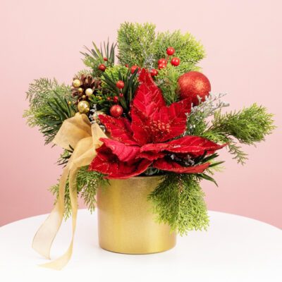 Red poinsettia Christmas arrangement with festive greens, berries, pine cones, and ornaments in a gold vase.