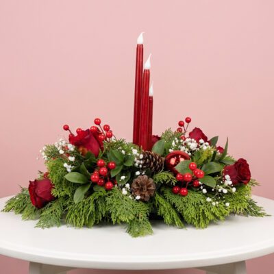 Red led candle Christmas centerpiece with red roses, berries, pine cones and festive greenery.