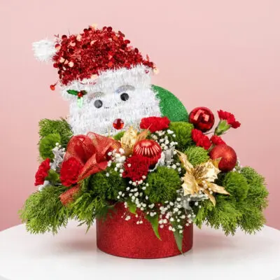 Santa themed Christmas arrangement featuring vibrant red flowers, gold poinsettias, lush greens, and Christmas ornaments—perfect for brightening homes, parties, and holiday celebrations.