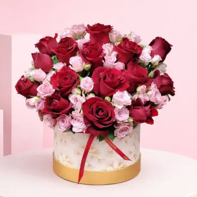 Rose Duo Box Deep with red roses and soft pink spray roses in a premium white-and-gold hatbox arrangement, finished with a satin ribbon.