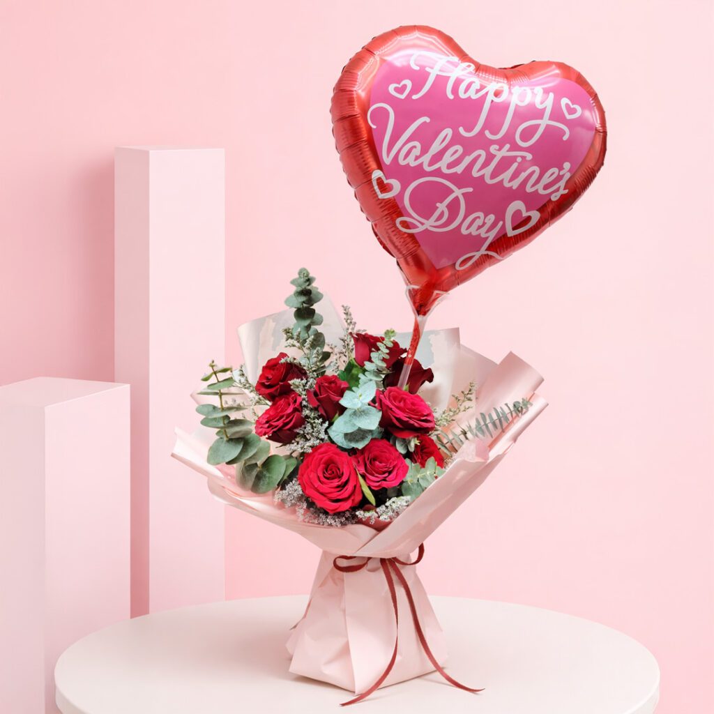 Red roses bouquet with heart balloon and green foliage wrapped in pink paper and a Happy Valentine’s Day heart-shaped balloon