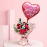Red roses bouquet with heart balloon and green foliage wrapped in pink paper and a Happy Valentine’s Day heart-shaped balloon