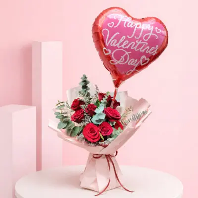 Red roses bouquet with heart balloon and green foliage wrapped in pink paper and a Happy Valentine’s Day heart-shaped balloon