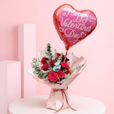 Red roses bouquet with heart balloon and green foliage wrapped in pink paper and a Happy Valentine’s Day heart-shaped balloon