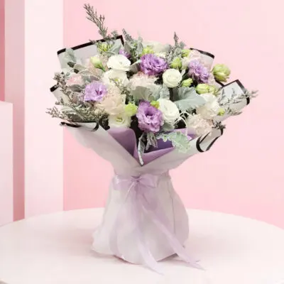 Handheld pastel flower bouquet with lavender whisper, white, and blush blooms wrapped in elegant paper with ribbon.