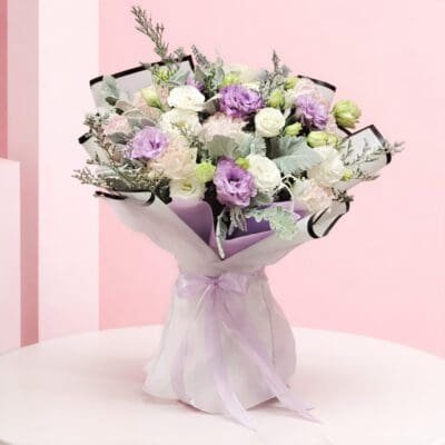 Handheld pastel flower bouquet with lavender whisper, white, and blush blooms wrapped in elegant paper with ribbon.