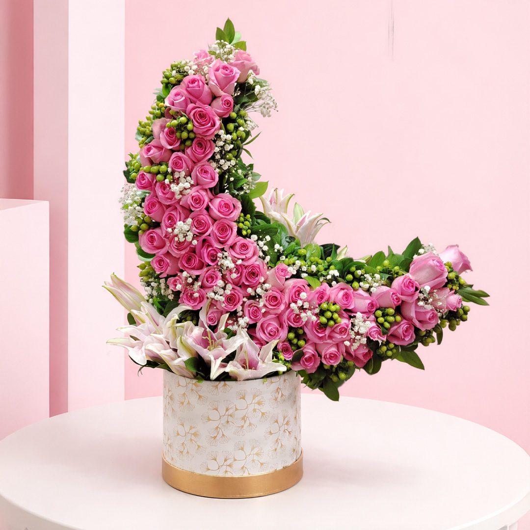 01 crescent bloom luxe consists of Pink roses are arranged in a crescent/curved design along with calla lilies and fillers in a decorative box