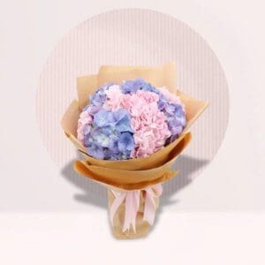 A colorful bouquet featuring pink and blue flowers, elegantly presented in a rustic paper bag.