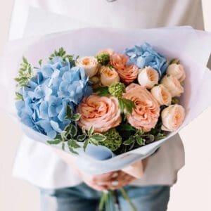A woman holds a vibrant bouquet of blue and pink flowers, showcasing a mix of colors and textures.