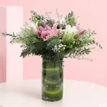 Cylindrical shaped glass vase filled with 6 rose lily stems, delicate baby's breath, and fresh foliage.