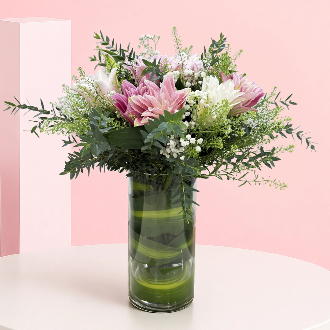 6-rose-lily-floral-vase Cylindrical shaped glass vase filled with 6 rose lily stems, delicate baby's breath, and fresh foliage.