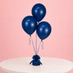 Three navy blue balloons tied with curly ribbon to a decorative weight, displayed on a white table.