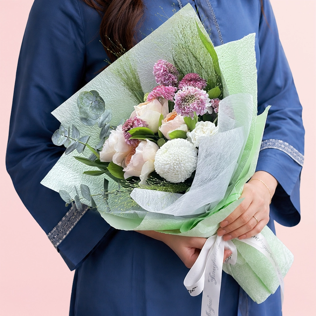 peach-rose-white-bloom-bouquet A mixed arrangement with peach roses, white ping pong chrysanthemum, white carnation, fresh fillers, and greenery wrapped as a bouquet.