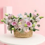 A handcrafted floral basket featuring pink roses, lisianthus, veronica, scabiosa blooms, and vibrant foliage in a naturally flowing arrangement.